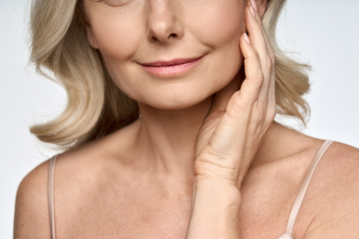 Face close up portrait of happy mid age 50 years old woman touching face with hand. Advertising of skin care anti wrinkle products for facial bottom part, lips, chin neck and decollete. Skin Tightening in Savannah, GA
